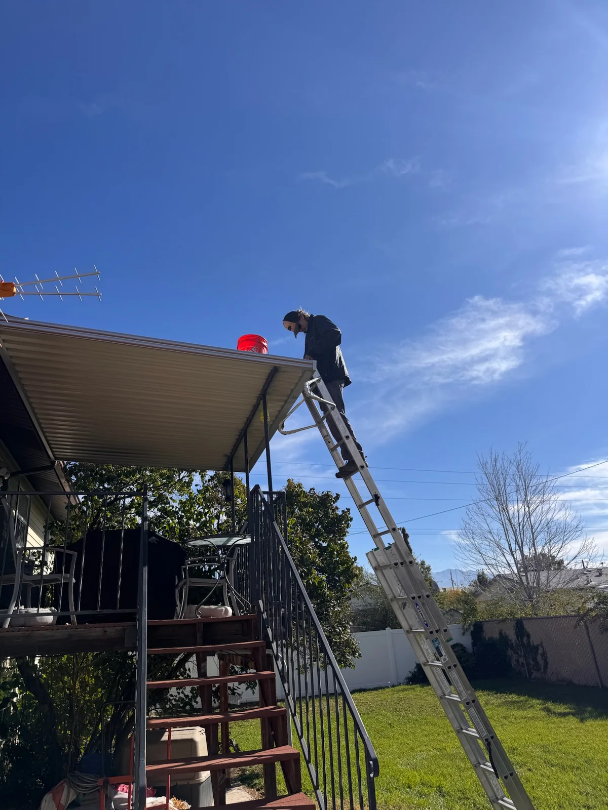 Clearly Clean technician cleaning a residential gutter from a ladder