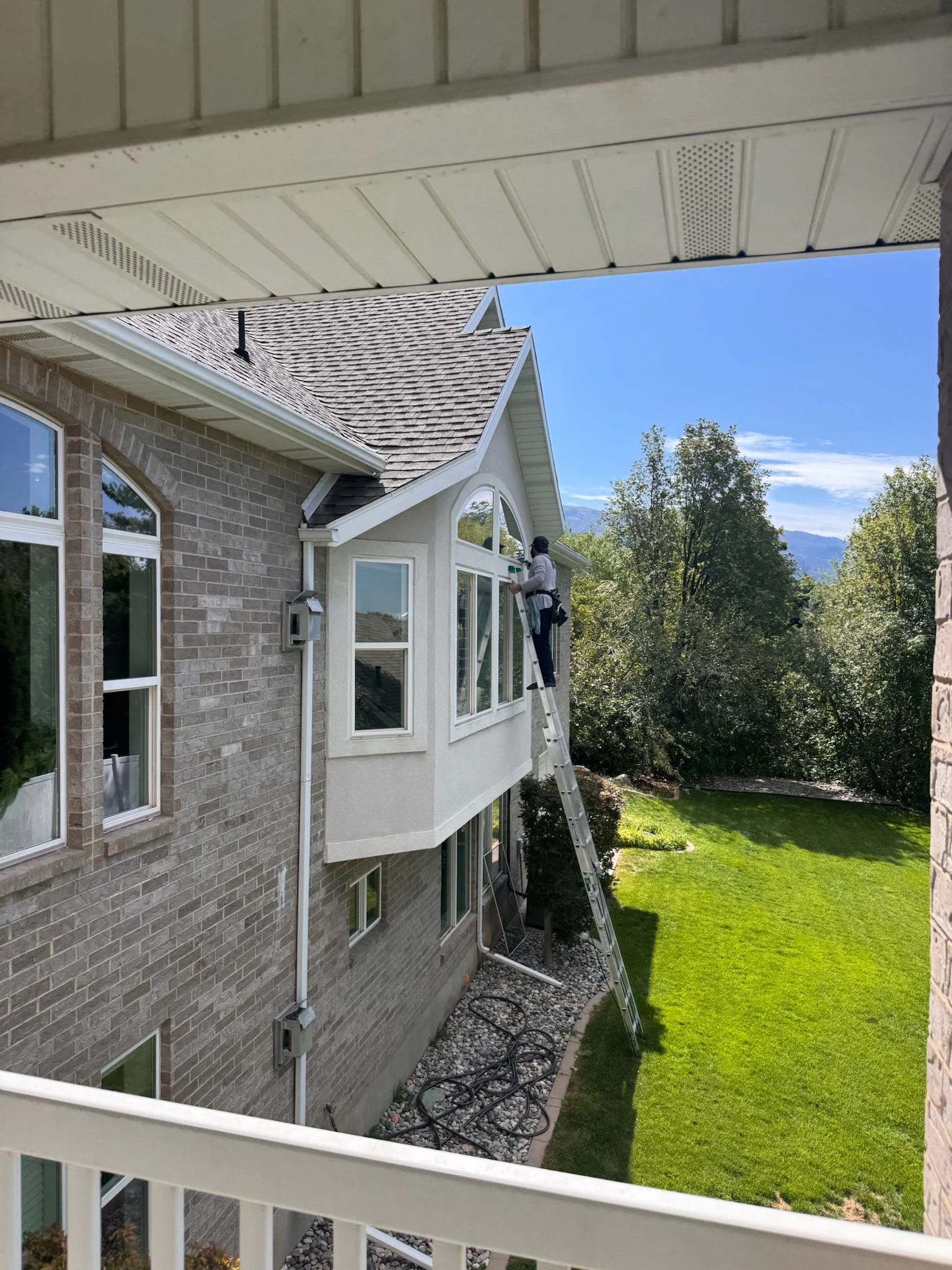 Clearly Clean technician cleaning upper-story residential windows on a Northern Utah home