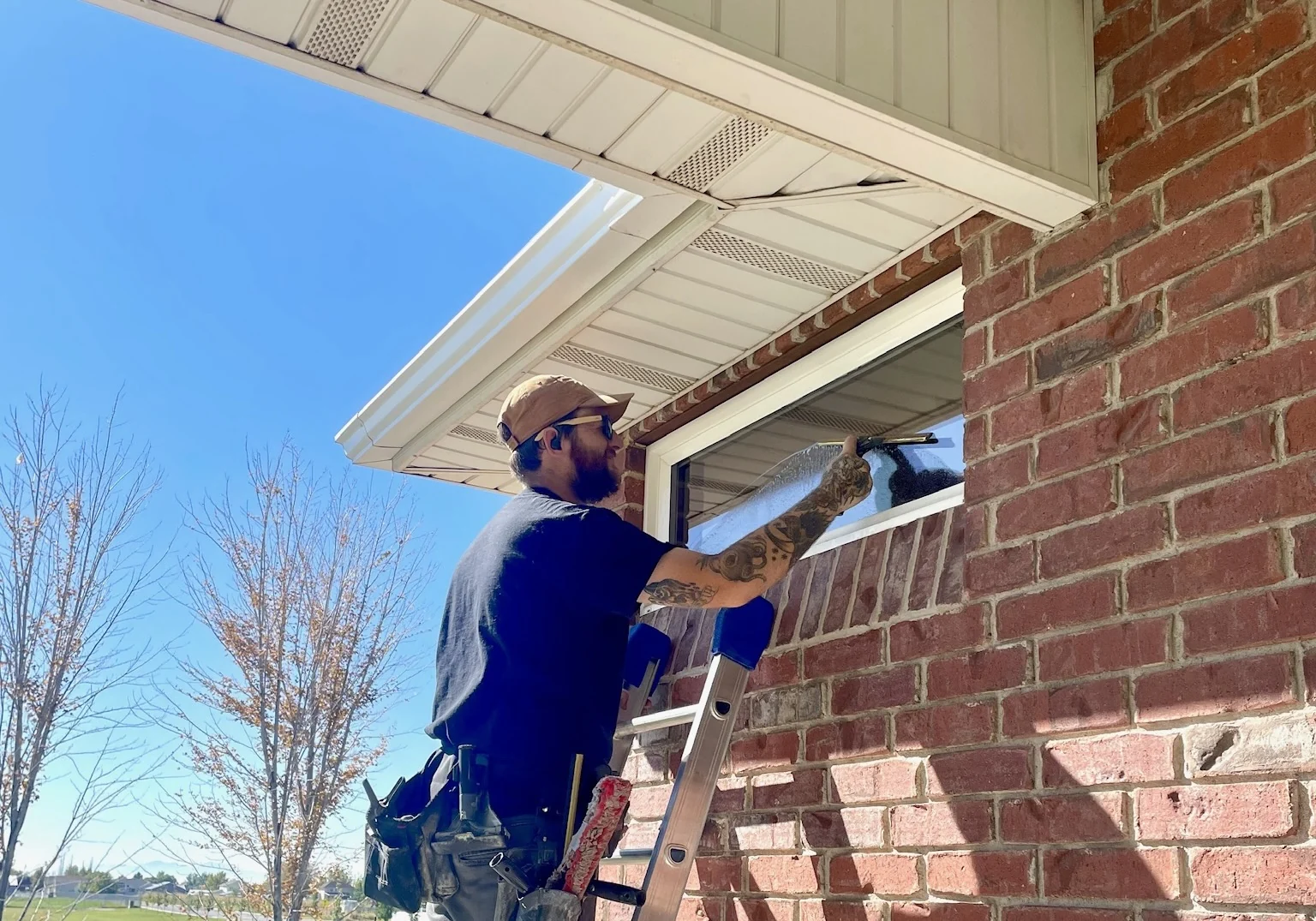 Clearly Clean technician cleaning a residential window with a squeegee from a ladder